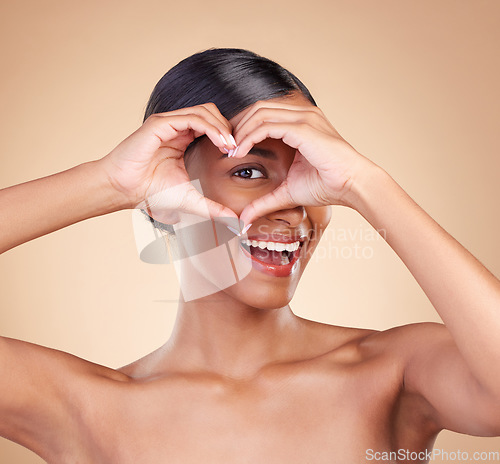 Image of Portrait, heart and hand gesture with a woman in studio on a beige background for beauty or skincare. Face, hands and emoji with an attractive young female posing for cosmetics or luxury wellness