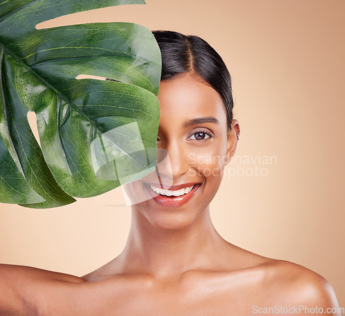 Image of Portrait, beauty and palm leaf with a model woman in studio on a beige background for natural skincare. Face, plants and nature with an attractive young female posing for cosmetics or luxury wellness