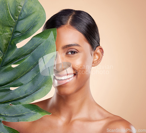 Image of Portrait, skincare and palm leaf with a model woman in studio on a beige background for natural beauty. Face, plants and nature with an attractive young female posing for cosmetics or luxury wellness