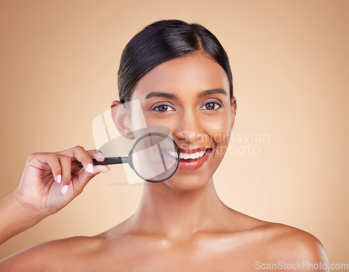 Image of Portrait, skincare and magnifying glass with a model woman in studio on a beige background searching for beauty. Face, investigation and smile with an attractive female looking for luxury cosmetics
