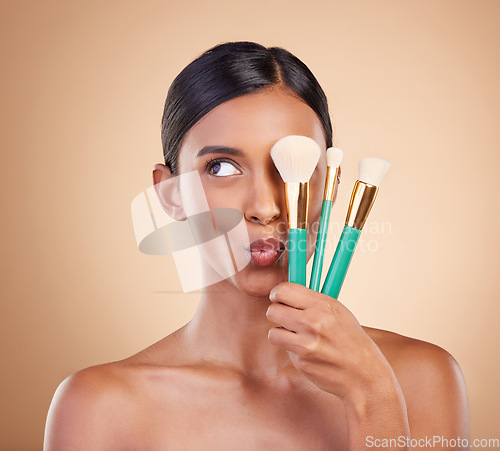 Image of Skincare, brush and Indian woman with makeup, foundation and funny on brown studio background. Female, lady or cosmetics tools with glamour, elegant or beauty for luxury grooming or facial expression