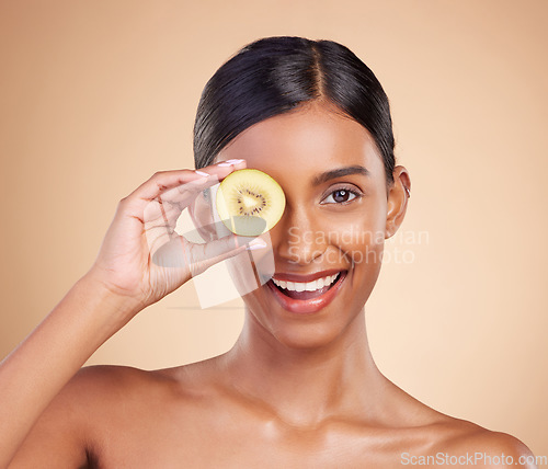 Image of Portrait, beauty and kiwi with a model woman in studio on a beige background to promote skincare. Face, eye and fruit with an attractive young female posing for organic, natural or luxury cosmetics