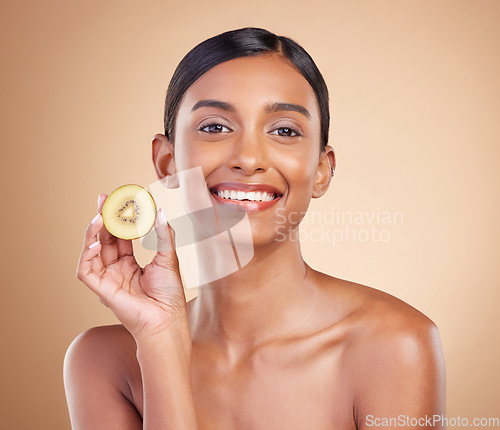 Image of Portrait, skincare and kiwi with a model woman in studio on a beige background to promote beauty. Face, fruit and natural with an attractive young female posing for organic or luxury cosmetics