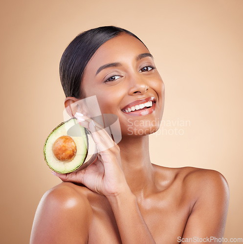 Image of Portrait, skincare and avocado with a model woman in studio on a beige background for beauty. Face, fruit and antioxidants with an attractive young female posing for organic or natural cosmetics