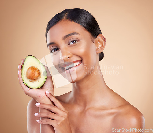 Image of Portrait, beauty and avocado with a woman in studio on a beige background to promote skincare. Face, fruit and antioxidants with an attractive young female posing for organic or natural cosmetics