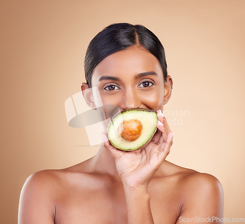 Image of Portrait, skin or avocado with a model woman in studio on a beige background to promote beauty. Face, eyes and fruit with an attractive young female posing for organic, natural or luxury antioxidants