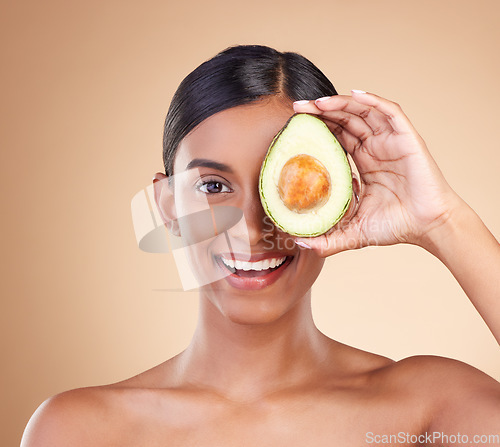 Image of Portrait, beauty and avocado with a model woman in studio on a beige background to promote skincare. Face, eye and fruit with an attractive young female posing for organic or natural antioxidants