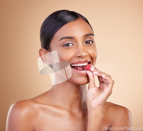 Image of Portrait, beauty and woman biting a strawberry in studio on a beige background to promote skincare. Face, fruit and eating with an attractive young female posing for organic or natural cosmetics