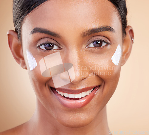 Image of Portrait, face and cream with a model woman in studio on a beige background closeup for skincare. Beauty, facial and lotion with an attractive young female smiling for antiaging cosmetic treatment