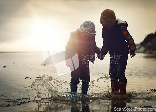 Image of Beach, sunset and silhouette of children in water splash together, holding hands and playing in waves. Fun, holiday and brothers, happy in boots on ocean vacation, jumping in sea on winter evening.