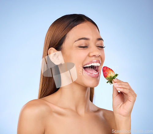 Image of Skincare, health and female with a strawberry in studio with a wellness, natural and face routine. Happy, beauty and woman model eating red fruit for nutrition, diet and self care by blue background.