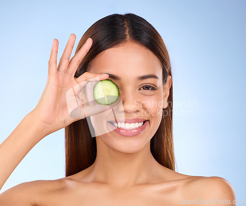 Image of Beauty, woman and cucumber for face portrait with a smile and dermatology skincare cosmetic. Female model on blue background for self care, facial glow and vegetable for natural skin health in studio