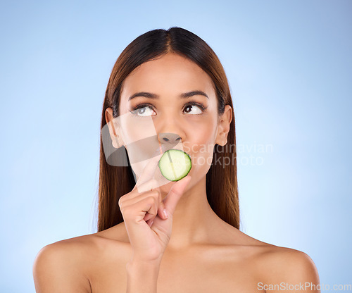 Image of Cucumber, woman and skincare face portrait with beauty and dermatology cosmetics. Female model on a blue background thinking about self care, facial glow and healthy fruit for natural skin in studio