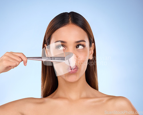 Image of Beauty, makeup and brush on nose of woman in studio for cosmetics, tools and self care. Glow, foundation and blush with girl model on blue background for facial, powder and cosmetology product