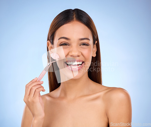 Image of Beauty, skincare and hispanic woman with facial roller and smile for anti aging glow on blue background. Cosmetics, skin repair and model rolling face with rose stone quartz product in studio promo.