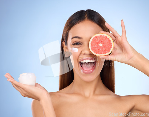 Image of Woman, moisturizer cream and grapefruit for natural skincare beauty and vitamin C against blue studio background. Portrait of happy female holding fruit, creme or lotion for healthy organic products