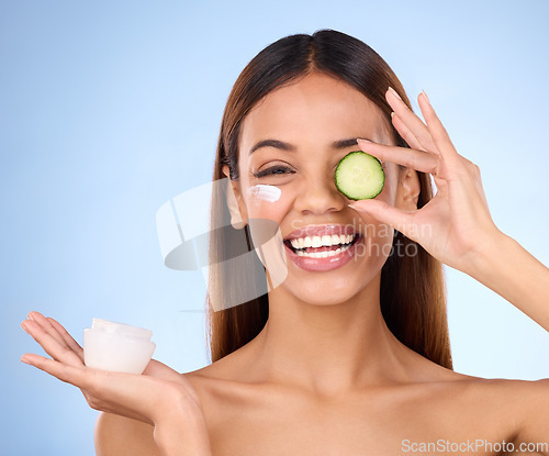 Image of Woman, moisturizer cream and cucumber for natural skincare, beauty and cosmetics against blue studio background. Portrait of happy female holding vegetable, creme or lotion for healthy organic facial