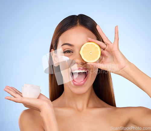 Image of Woman, moisturizer cream and lemon for natural skincare, beauty and vitamin C against blue studio background. Portrait of happy female holding citrus fruit, creme or lotion for healthy organic facial