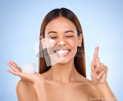 Image of Woman, face and moisturizer cream for beauty skincare cosmetics, self love or care against blue studio background. Happy female with lotion or moisturizing creme for perfect skin or facial treatment