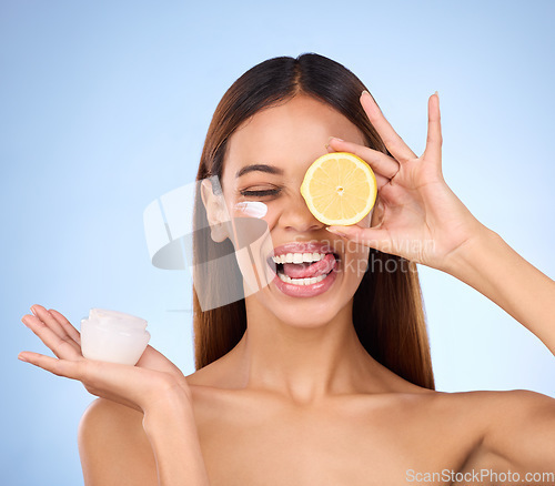 Image of Woman, moisturizer cream and lemon for natural skincare, beauty and vitamin C against a blue studio background. Female holding citrus fruit, creme or lotion for healthy organic nutrition or facial