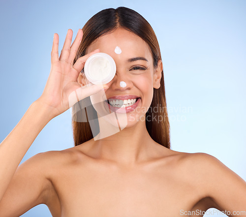 Image of Woman, portrait and face with moisturizer cream for beauty skincare cosmetics, self love or care against blue studio background. Happy female with lotion or moisturizing creme for facial treatment