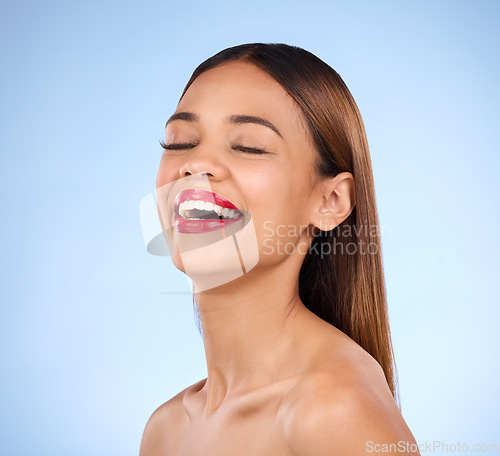 Image of Beauty, woman and red lipstick makeup while laughing with cosmetics on face in studio. Happy aesthetic female model person on a blue background for self care, facial glow and shine or color for skin
