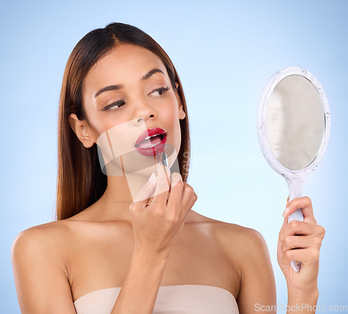 Image of Beauty, woman and red lipstick or makeup with mirror in hand for face cosmetic product in studio. Aesthetic female model on a blue background with color application on lips for shine and self care