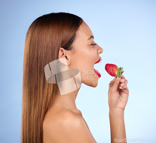 Image of Beauty, wellness and profile of woman with strawberry on blue background for diet, nutrition and healthy eating. Skincare, happy and girl with fruit in studio for cosmetics, makeup and natural snack