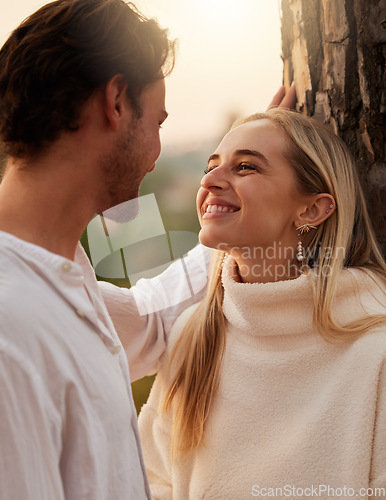 Image of Happy, love and couple by tree in nature at sunset for romance, bonding and quality time together. Romantic, dating and man and girl show affection on holiday, honeymoon vacation and relax on weekend