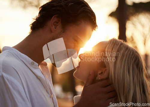 Image of Couple, love and kiss outdoor at sunset for love, care and romance with hands on face on a date. Young man and woman together on valentines day with lens flare, peace and freedom in nature forest