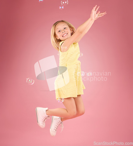 Image of Child, jump and bubbles for a smile portrait in studio with a pink background for fun. Female kid model jumping with happiness, play and cheerful face isolated on gradient color and space