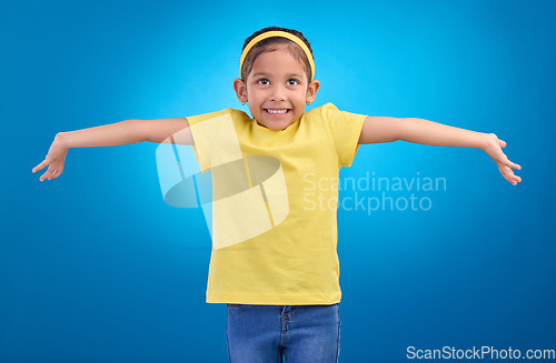 Image of Girl, child and happy or shrugging or unsure in studio with arms and hands stretched with a smile. Kid on blue background clueless, doubt and confused about question or reaction with hand gesture