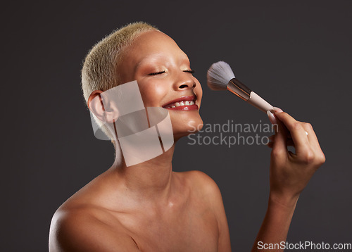 Image of Woman, smile and makeup brush for facial beauty cosmetics, skincare or treatment against a gray studio background. Happy beautiful female model applying cosmetic product on face for self care or love