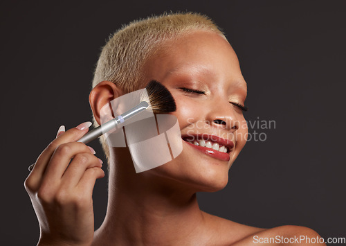 Image of Woman, smile and makeup brush for beauty cosmetics, skincare or facial treatment against a gray studio background. Happy beautiful female model applying cosmetic product on face for self care or love