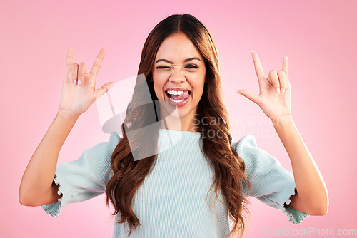 Image of Portrait of woman, rock hand gesture and wink in studio, heavy metal expression on face and pink background. Crazy, wild hispanic model and hands in devil horn sign with punk attitude and happy smile