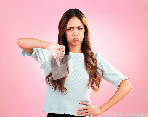 Image of Sad, thumb down and portrait of a woman in a studio with an upset, moody or disappointed face. Loser, unhappy and young female model posing with a angry hand gesture isolated by a pink background.