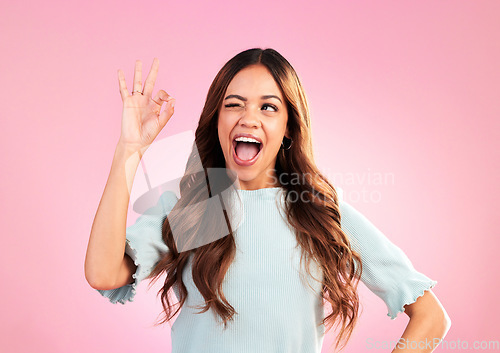 Image of Wink, studio and woman with a perfect hand gesture, excitement and positive face expression. Happy, smile and young female model from Colombia with a ok sign language isolated by a pink background.