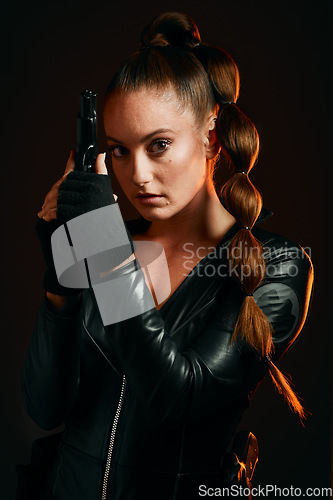 Image of Portrait, gun and spy with a woman assassin in studio on a dark background ready for combat. Hero, leather and power with an attractive young female secret agent holding a weapon on a mission