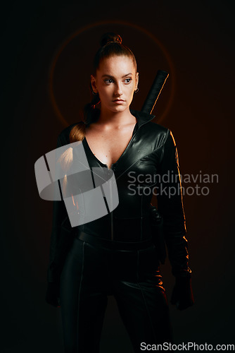 Image of Woman, warrior and fashion outfit in studio for action, fight and safety from danger in a dark studio. Strong female model, assassin or killer in scifi leather cosplay costume with weapon for action