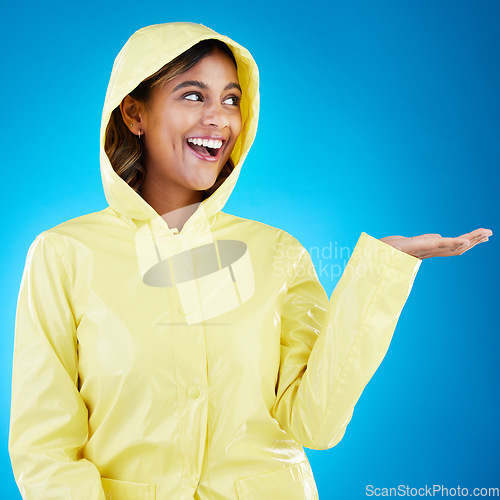 Image of Hand, rain and happy woman in studio excited for weather, drop or storm while posing on gradient blue background. Smile feeling and girl enjoy rainfall, splash and winter season, cheerful or isolated
