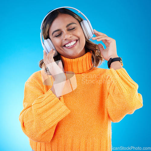 Image of Music headphones, smile and woman in studio isolated on a blue background. Podcast, radio and happy Indian female with eyes closed streaming, listening and enjoying sound, audio or song with headset.
