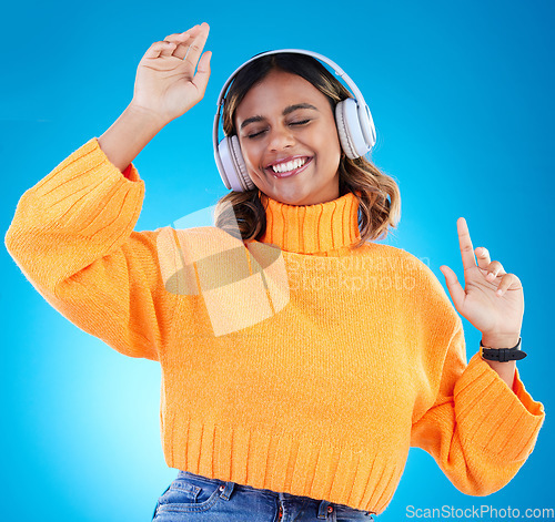 Image of Music headphones, smile and woman dance in studio isolated on a blue background. Dancing, radio and happy Indian female with eyes closed streaming, listening and enjoying sound, audio podcast or song