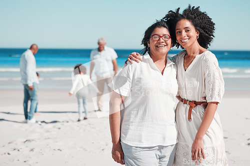 Image of Portrait, summer with a mother and daughter on the beach during summer while their family play in the background. Love, smile or nature with a senior woman and adult child bonding outdoor together