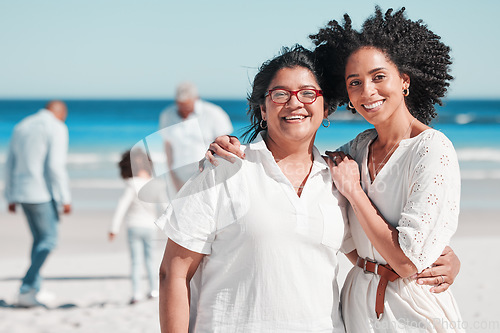 Image of Portrait, nature with a mother and daughter on the beach during summer while their family play in the background. Love, smile or summer with a senior woman and adult child bonding outdoor together