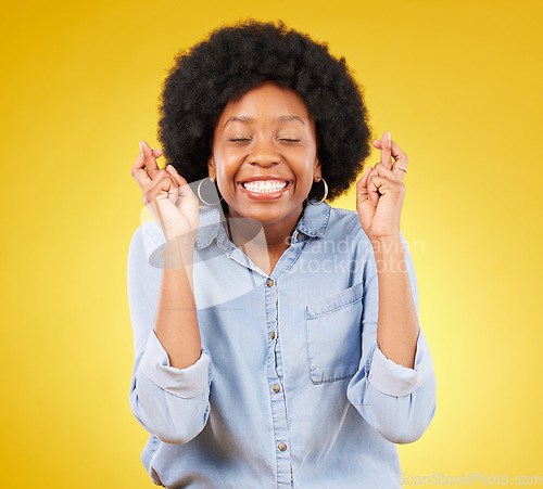 Image of Happy, smile and fingers crossed by black woman in studio for wish, hope and good luck against yellow background. Eyes closed, hand and emoji by excited female waiting, optimistic and hopeful gesture