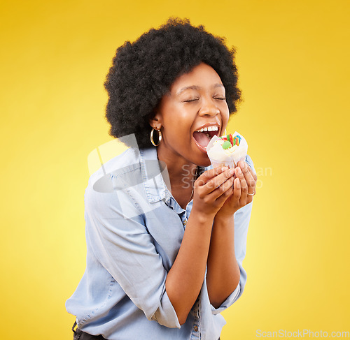 Image of black woman, cupcake and excited or happy in studio while eating sweet food on a yellow background. African female model with snack, dessert or cake for happiness, birthday or celebration mockup