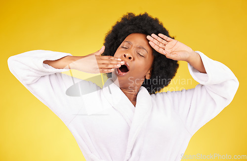 Image of Yawn, morning and wake up with a black woman in studio on a yellow background wearing a bathrobe. Relax, tired or rest with an exhausted young female yawning and stretching after sleeping