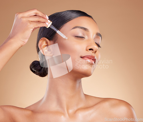 Image of Woman, dropper and retinol on face for skincare beauty or cosmetics against a studio background. Beautiful female with pipette applying oil drop to skin for hydration, moisturizer or facial treatment