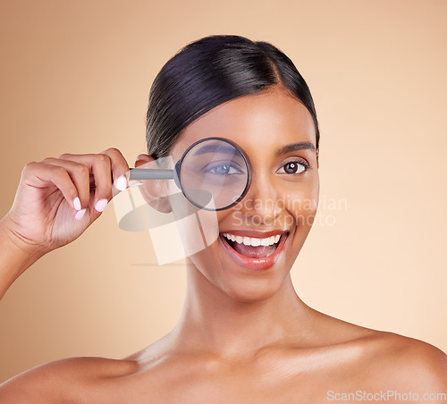 Image of Portrait, beauty and magnifying glass with a model woman in studio on a beige background searching for skincare. Face, eye and investigation with an excited young female looking for luxury cosmetics