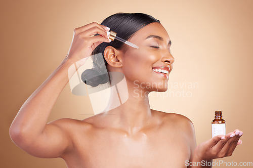 Image of Woman, dropper and retinol on face for skincare beauty or cosmetics against a studio background. Happy female model with smile applying oil drop to skin for hydration, moisturizer or facial treatment